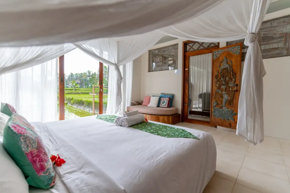 A canopy bed and wooden seating beside large windows