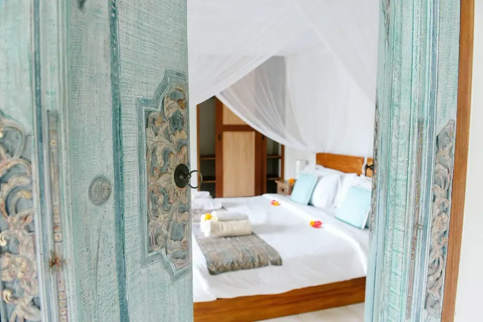 A canopy bed seen through carved pale-blue doors